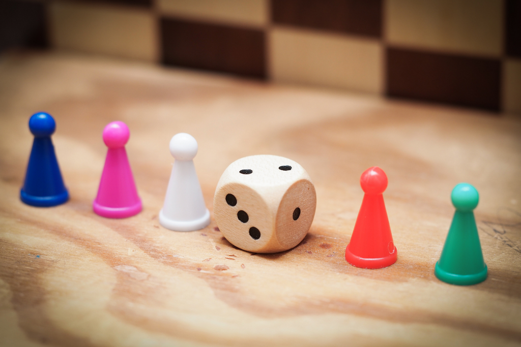 image shows 5 colourful playing pieces from a board game, there is a dice showing the number 2 in the middle of the pieces.