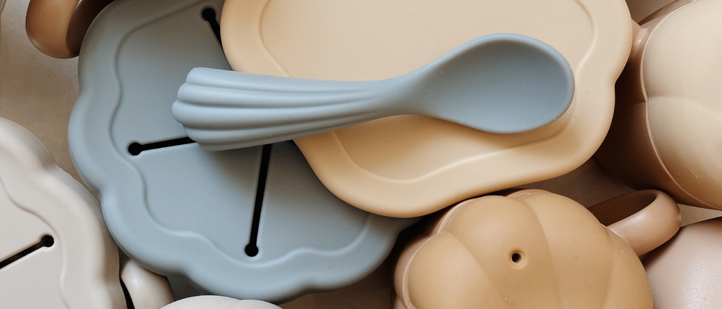 selection of silicone snack pots, cups and spoons from konges slojd in muted tones of blue. cream and sand.